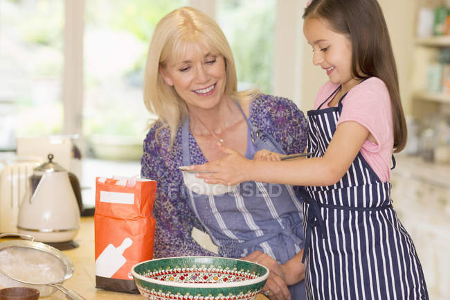 Grandmother and granddaughter baking sifting flour in kitchen — Stock Photo