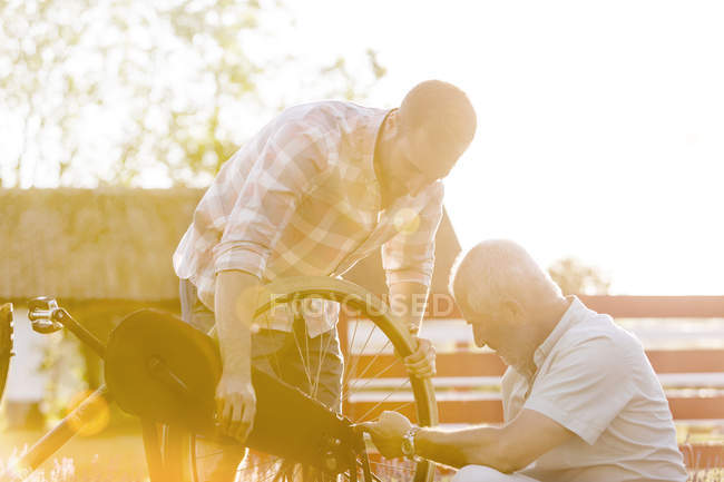 Отец и взрослый сын чинят велосипед — стоковое фото