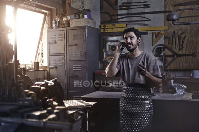 Blacksmith talking on cell phone in forge — Stock Photo