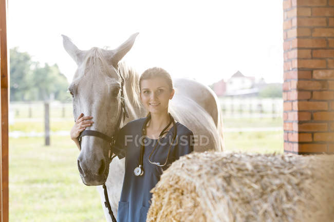Портрет усміхненого ветеринара з конем у сарай — стокове фото
