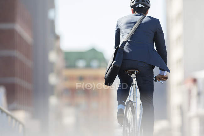 Businessman in suit and helmet riding bicycle in city — Stock Photo