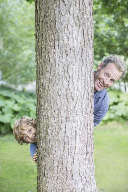 Padre e hijo mirando desde detrás del árbol - foto de stock