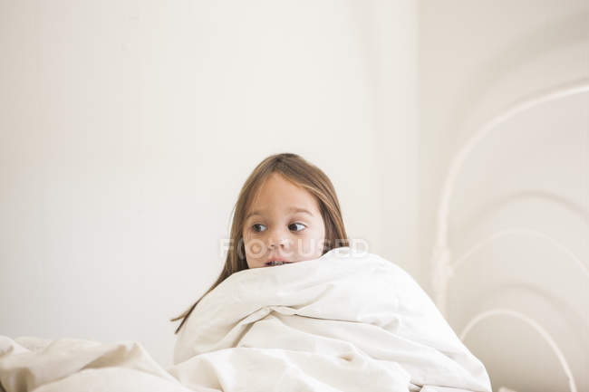 Toddler girl sitting up in bed under duvet — Stock Photo