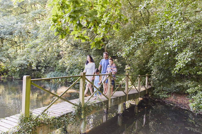 Family crossing footbridge in park with trees — Stock Photo