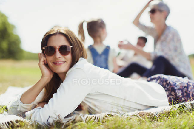 Portrait smiling woman laying on blanket in sunny field — Stock Photo