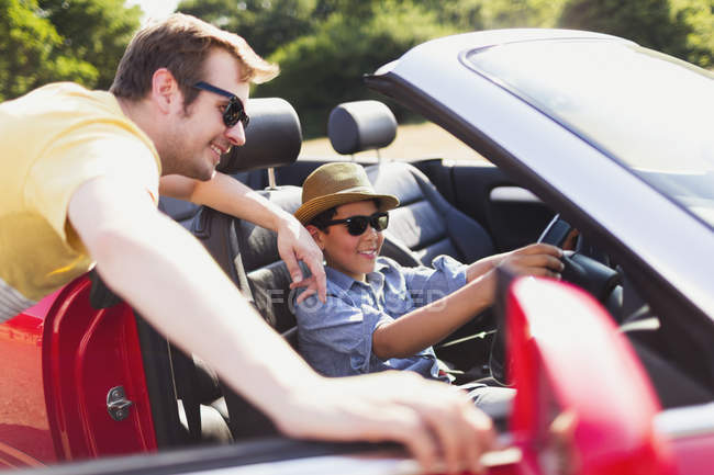 Father watching son pretend to drive in convertible — Stock Photo