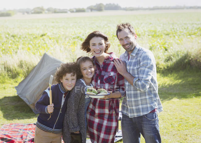 Portrait smiling family with barbecued hamburgers at sunny campsite — Stock Photo