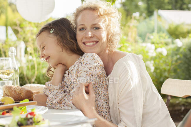 Мать и дочь улыбаются за столом на открытом воздухе — стоковое фото