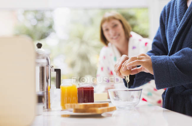 Женщина смотрит, как муж разбивает яйцо на кухне — стоковое фото