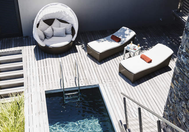 Lounge chairs on wooden deck by modern pool — Stock Photo