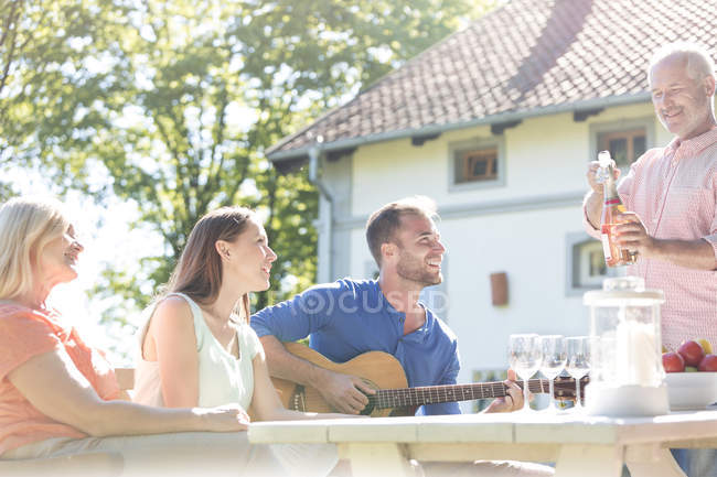 Pai abrindo garrafa de vinho rosa para a família na mesa do pátio ensolarado — Fotografia de Stock