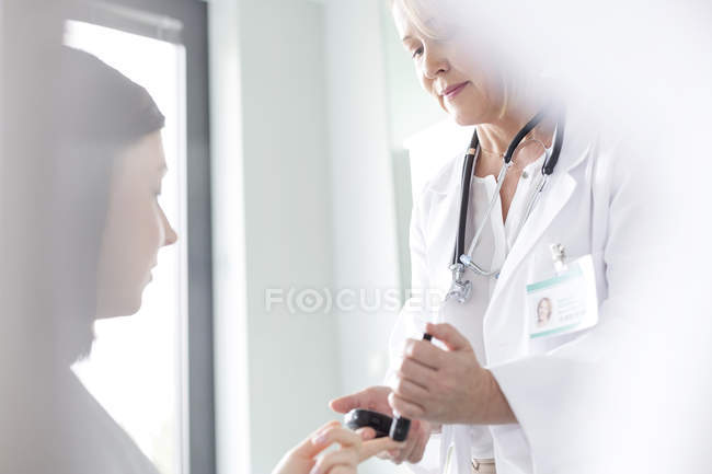 Médico que examina el azúcar en sangre del paciente para la diabetes en sala de examen - foto de stock