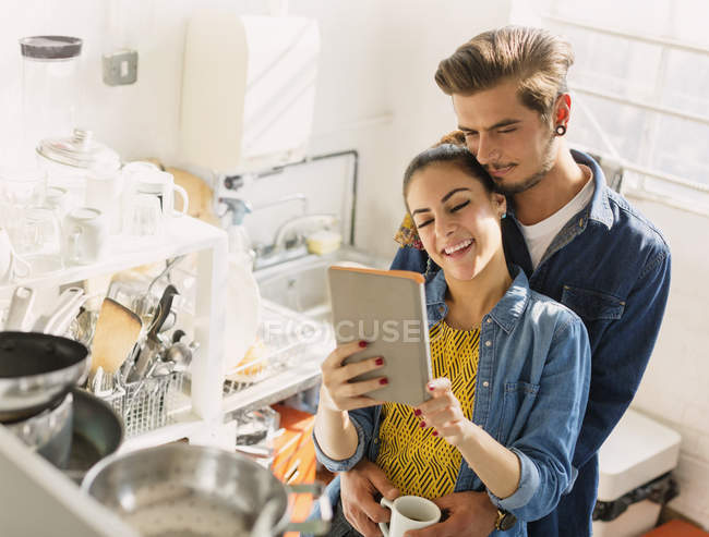 Pareja joven cariñosa usando tableta digital en la cocina del apartamento - foto de stock