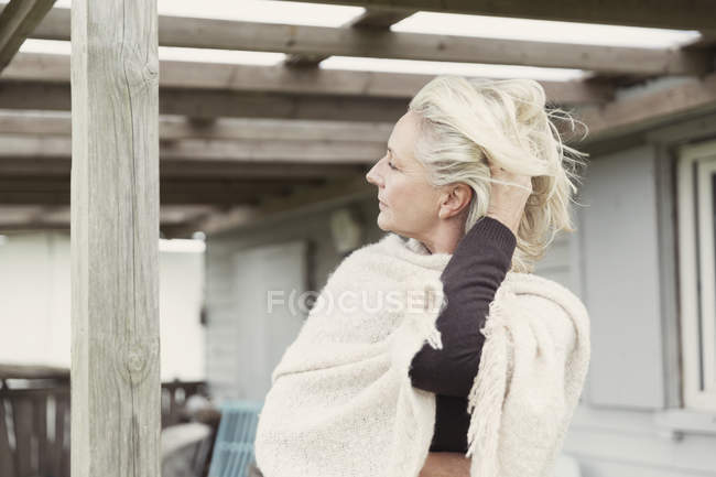Mujer mayor con la mano en el pelo con chal en el porche - foto de stock