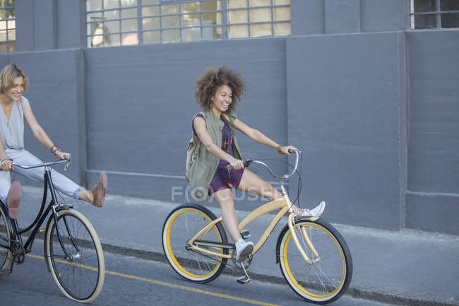 Donne giocose che costeggiano le biciclette lungo la strada urbana — Foto stock