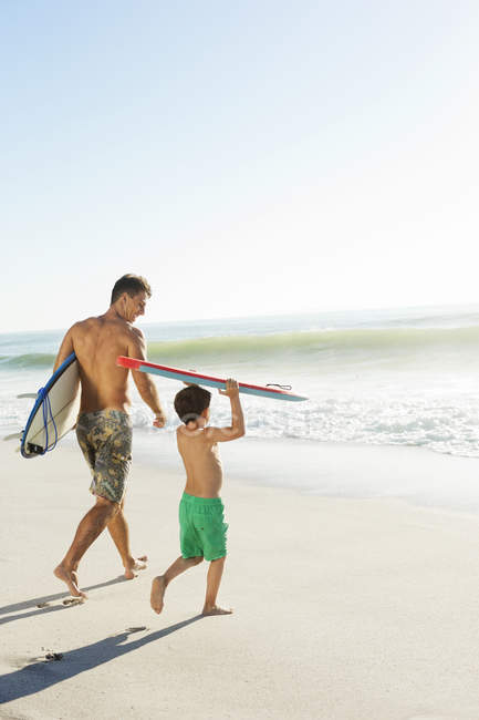 Padre e hijo llevando tabla de surf y bodyboard en la playa - foto de stock