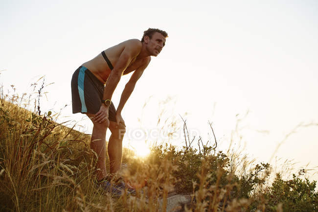 Tired male runner with hands on knees on grassy trail — Stock Photo