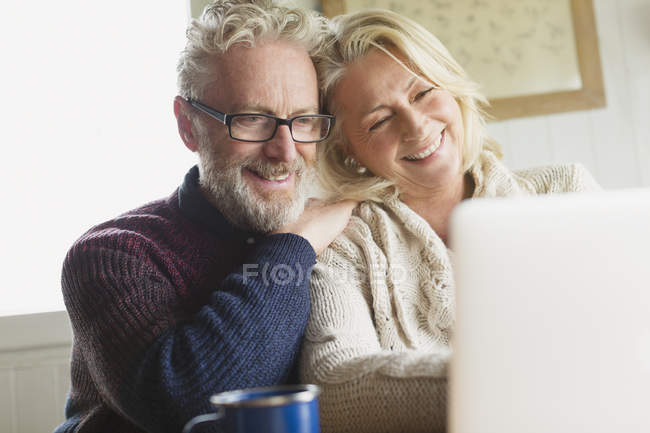 Sonriente pareja de personas mayores utilizando el ordenador portátil en la cocina - foto de stock