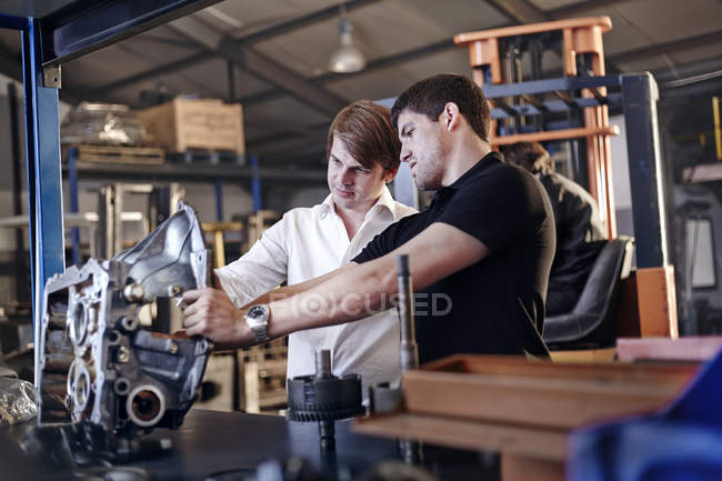 Mecánico y cliente examinando parte en taller de reparación de automóviles - foto de stock