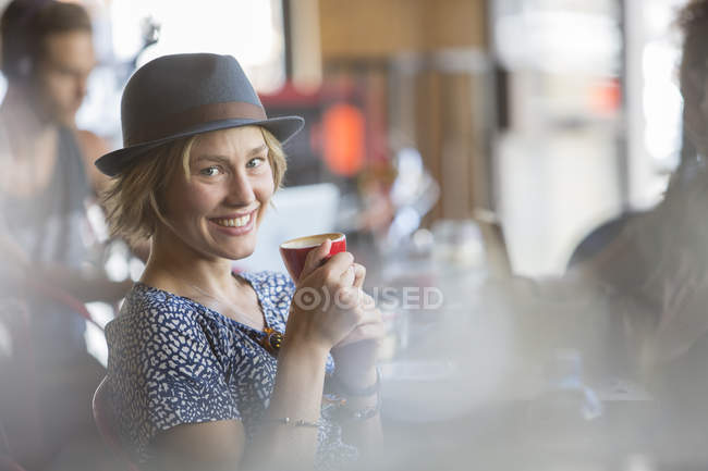 Retrato sonriente mujer en sombrero bebiendo espresso en la cafetería - foto de stock