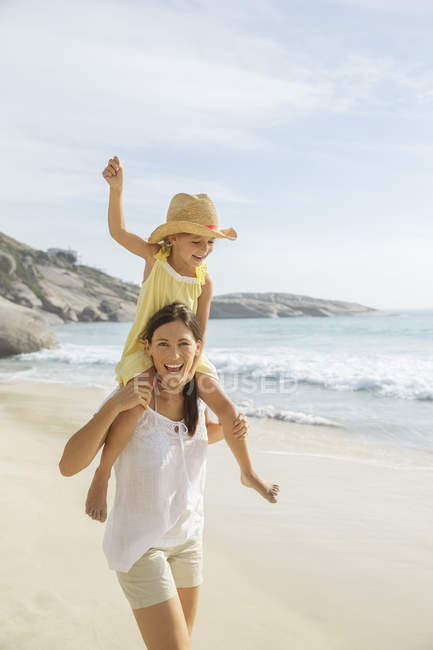 Mother carrying daughter on shoulders on beach — Stock Photo