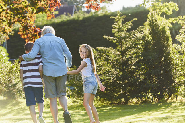 Portrait smiling girl walking with grandmother and brother in garden — Stock Photo