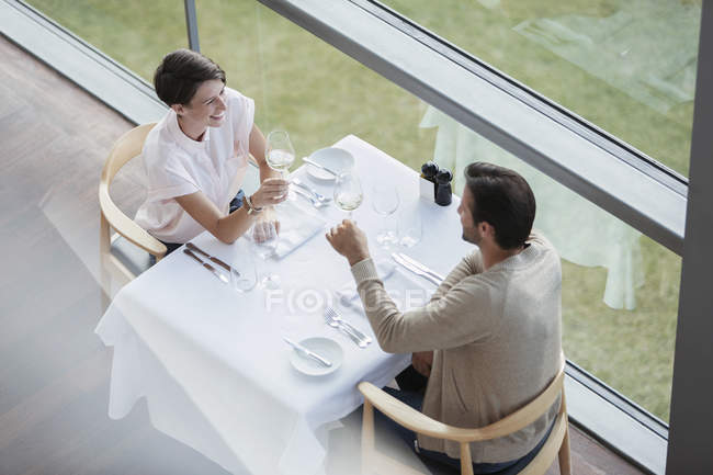 Un par de copas de vino tostadas en la mesa del restaurante en la ventana - foto de stock