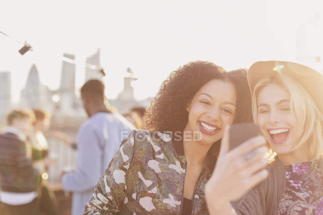 Enthusiastic young women taking selfie at rooftop party — Stock Photo