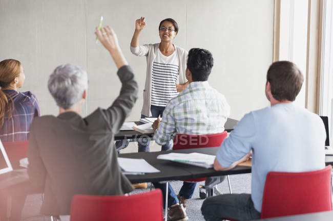 Profesor llamando a estudiante con mano levantada en aula de educación de adultos - foto de stock