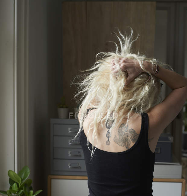 Mujer joven con las manos en el pelo revelando tatuajes de espalda - foto de stock