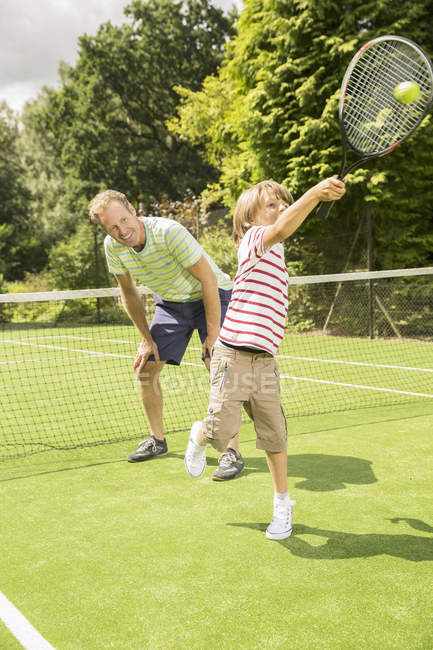 Padre e hijo jugando tenis en la cancha de hierba - foto de stock