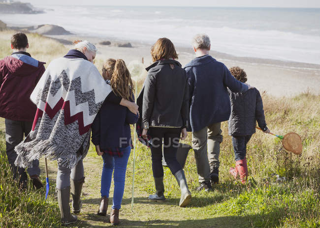 Familia multi-generación caminando por sendero de playa de hierba soleada - foto de stock