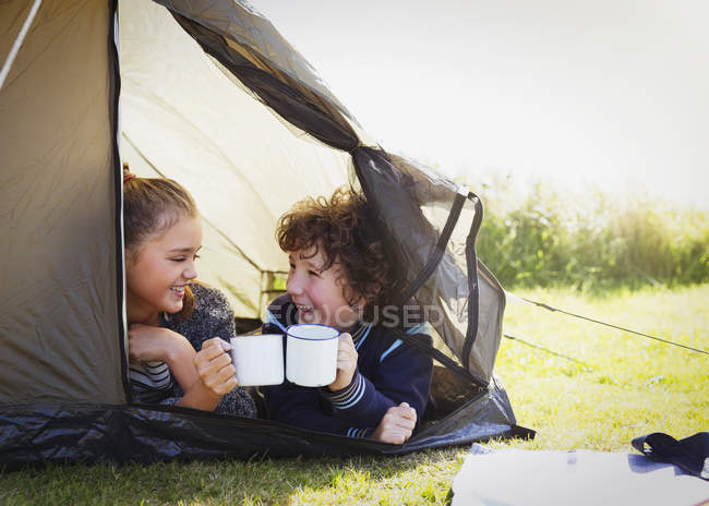 Brother and sister toasting mugs in tent — Stock Photo
