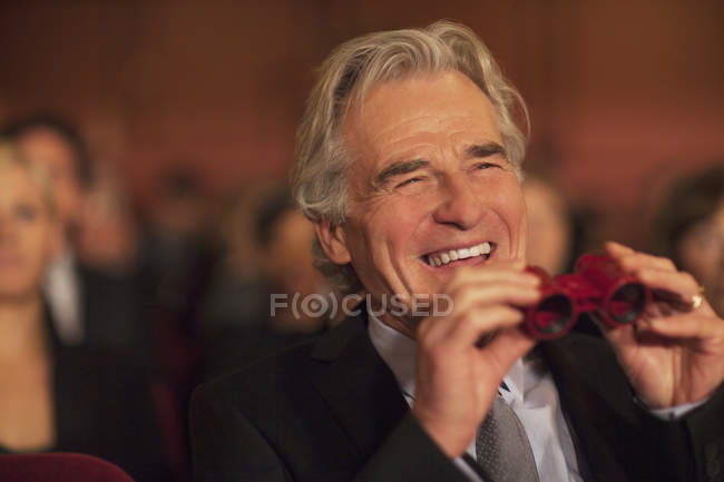 Man with opera glasses laughing in theater audience — Stock Photo