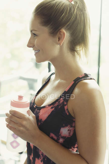 Усміхнена жінка п'є воду в спортзалі — стокове фото