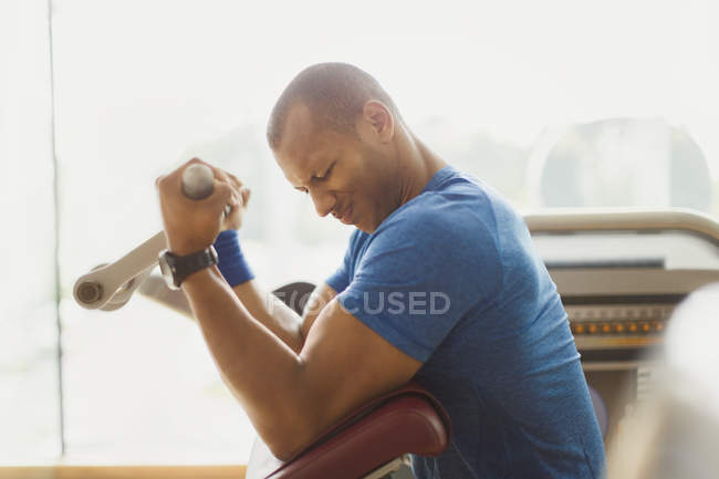 Homem fazendo bíceps cachos um equipamento de exercício no ginásio — Fotografia de Stock