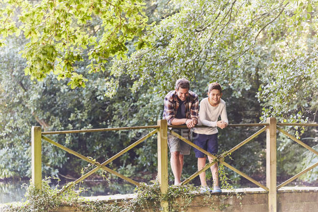 Padre e hijo de pie en el puente de madera sobre el río - foto de stock