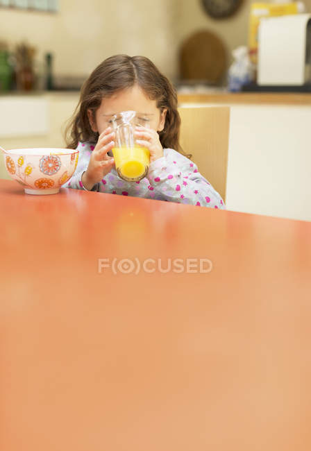 Menina bebendo suco de laranja na mesa de café da manhã — Fotografia de Stock