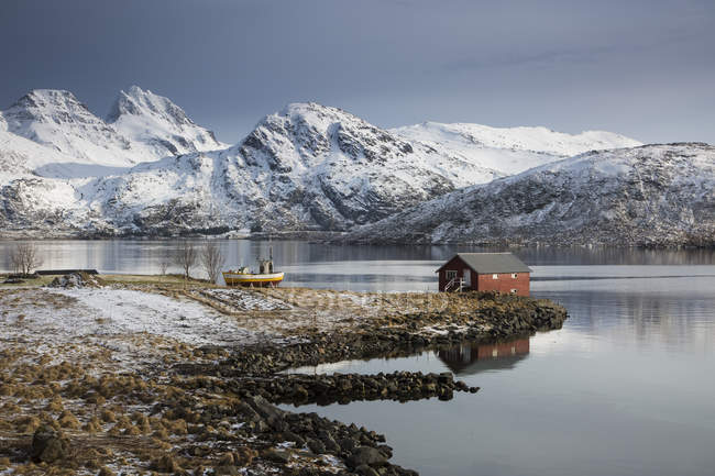Fischerhütte in kalter Bucht unter schneebedeckten Bergen, Norwegen — Stockfoto
