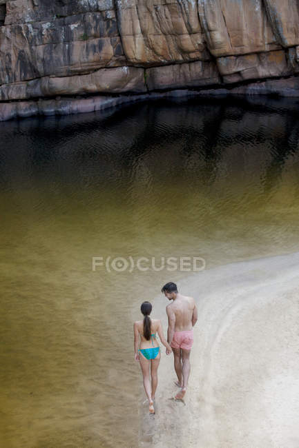 Couple marchant le long de la piscine contre le rocher — Photo de stock