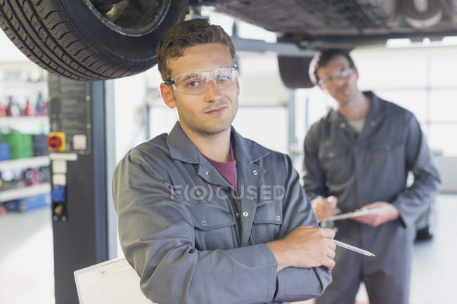 Portrait confident mechanic under car in auto repair shop — Stock Photo
