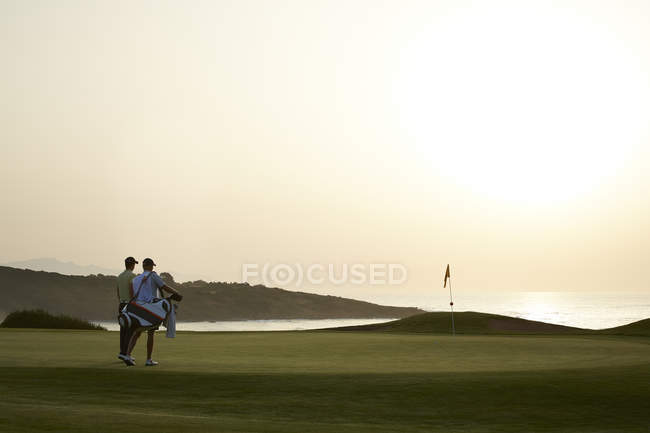 Visão traseira dos homens no campo de golfe ao pôr-do-sol — Fotografia de Stock