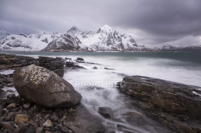 Montañas cubiertas de nieve detrás de un lago frío escarpado, Haukland Lofoten Islands, Noruega - foto de stock