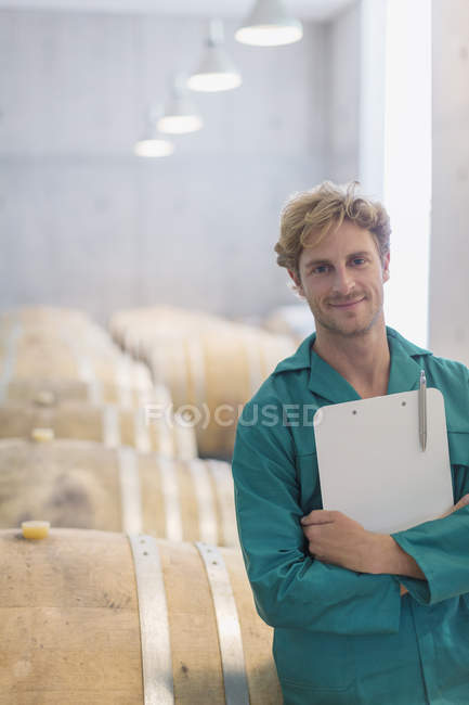Portrait smiling vintner with clipboard in winery cellar — Stock Photo