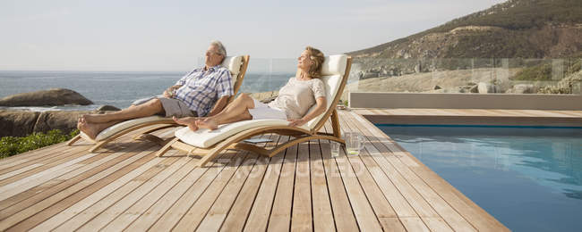 Casal mais velho relaxante em cadeiras de gramado por piscina — Fotografia de Stock
