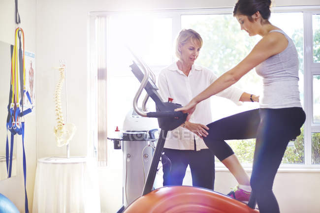 Physical therapist guiding woman on stationary bike — Stock Photo