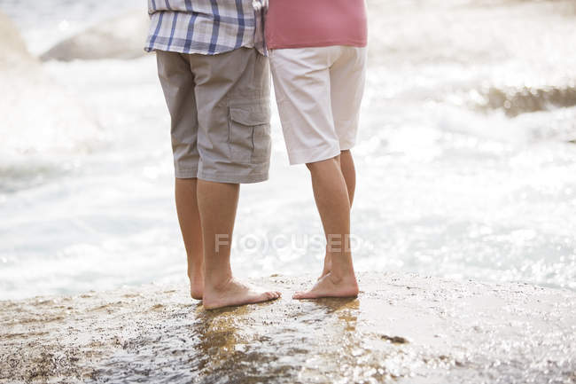 Coppia anziana in piedi sulla roccia in spiaggia — Foto stock