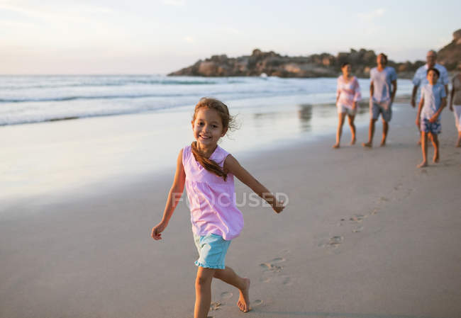 Девочка, гуляющая на пляже с семьей на заднем плане — стоковое фото