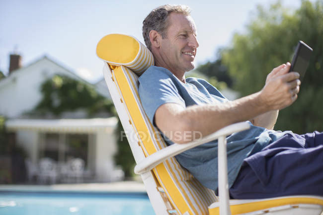 Homem lendo na cadeira lounge na beira da piscina — Fotografia de Stock