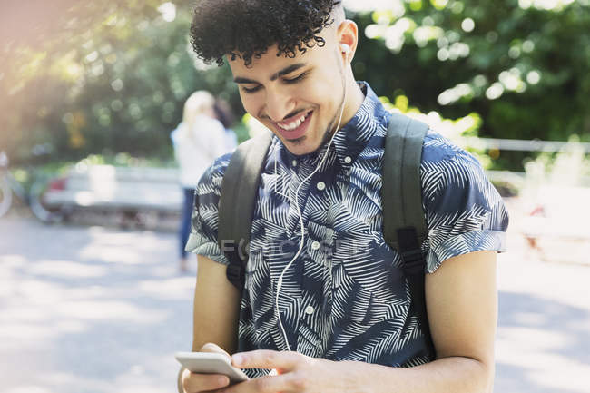 Homem sorridente com cabelo preto encaracolado ouvindo música com fones de ouvido e mp3 player — Fotografia de Stock